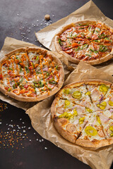 three beautiful colorful juicy different pizzas lie on parchment on a black background