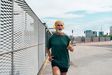 Active senior man listening to music and jogging by fence