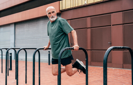 Active senior man exercising on parallel bars in front of building