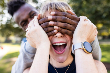 Surprised young woman with eyes covered by friend's hands at park