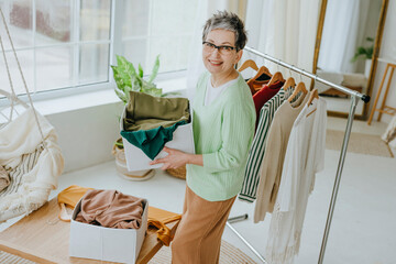 Woman holding box with old clothes near rack at home