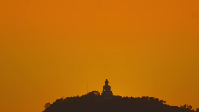 Stunning sky behind Phuket big Buddha on a hilltop at colorful sunset The sky was illuminated with shades of orange and red, creating a breathtaking view..Sunset with amazing light rays effects.