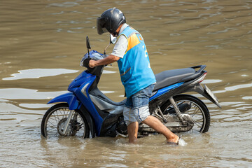 A moto-taxi driver pushes a motorbike through a flooded street, Thailand
