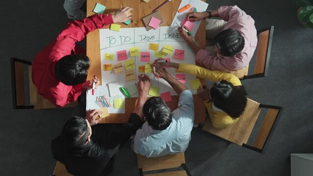 Top view of people writing and making scrum task board while writing marketing and planning strategy at colorful sticky notes. Smart team manage work performance by using kanaban board. Convocation.