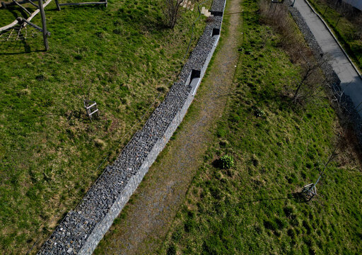 gabion retaining walls with pipes for drainage water into the gutter by the road. wooden benches inserted, built into a dry wall in the park