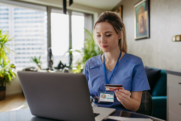Nurse paying bills online with debit or credit card, working on notebook. Doctor in uniform shopping online, Work-life balance for healthcare worker. - obrazy, fototapety, plakaty