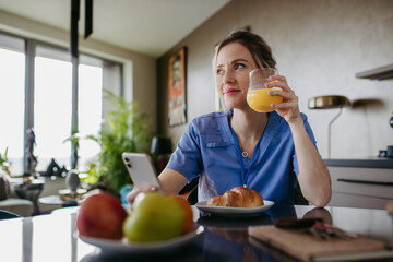 Female nurse or doctor getting ready for work in the morning, scrolling on smartphone while eating...