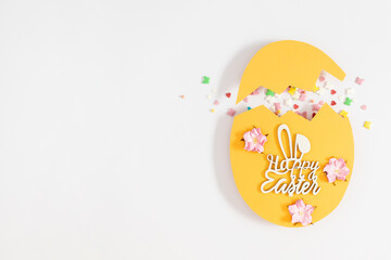 Easter decor concept. Frame made in shape of an Easter egg with colorful Easter eggs and sugar sprinkled candies on white background.Top view. Flat lay.