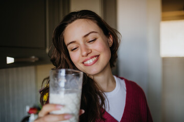 Beautiful woman drinking glass of plant-based milk in the kitchen.