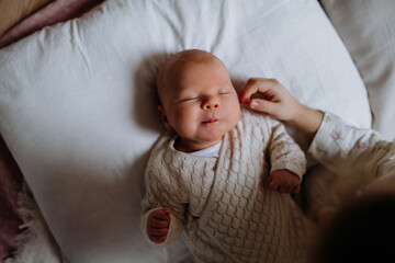 Top view of cute little baby sleeping in bed, big sister stroking newborn cheek. Sisterly love, joy for new family member.