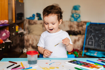 Happy cheerful child draws with a brush in an album using multi-colored paints