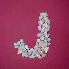 Letter J made of white stones. Creative alphabet concept on a red background. 