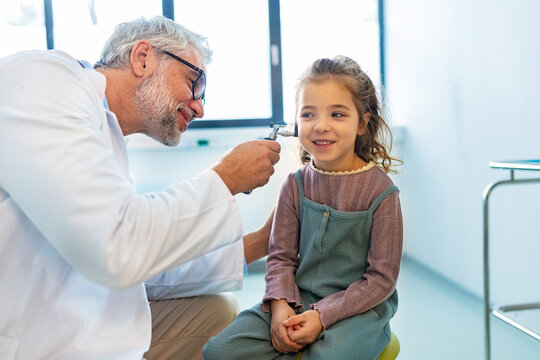 Doctor examining little girl's ear using otoscope, looking for ear infection. Friendly relationship between the doctor and the child patient.
