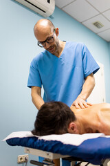 Vertical photo of a physical therapist or chiropractor in blue uniform performing rehabilitation on...