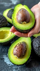 Creamy avocado held in hand, selection of avocados on blurred background with copy space
