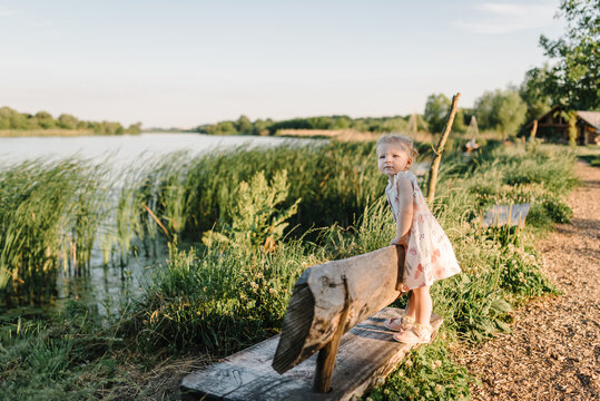 Child walking outdoors. A happy family with children is sitting on bench on shore of lake at sunset. Girl in the summer park.