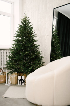 Beautiful New Year home decor, Christmas tree with lights next to a white armchair