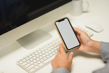 Closeup female office worker holding smartphone with empty screen sitting at her workplace