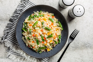 Top view of dark grey plate with hot fried long rice and vegetables, green beans, carrot, bell pepper.