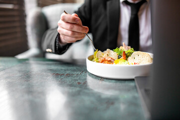 person savoring a fresh salad at a stylish green table. The individual, dressed in formal attire, uses a fork to enjoy the colorful mix of leafy greens, vegetables, and bread. - obrazy, fototapety, plakaty