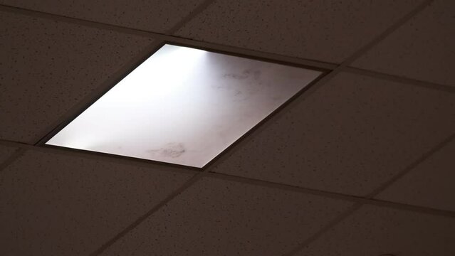 Low angle handheld shot of white lamp glowing on tiled ceiling over room