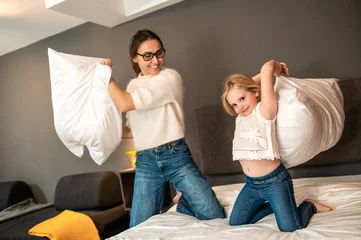 Fotobehang Mother and her little daughter playing with cushions on bed in hotel room © zinkevych