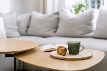 Cup of tea and fresh french croissant on coffee table near sofa in living room - obrazy, fototapety, plakaty