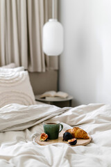 Selective focus on plate with cup of coffee, croissant and fruit on hotel bed