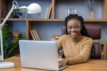 Woman remote worker in glasses with dreadlocks sitting at workplace with laptop in home office