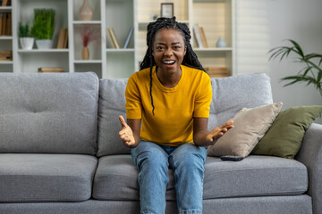 Young woman in yellow tshirt sitting on the sofa and looking excited