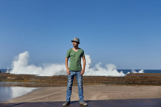 Man in casual attire stands on a pier with large waves breaking in the background under a blue sky. Tenerife, Spain