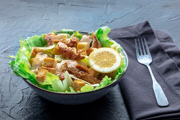 Caesar salad with chicken breast, lettuce, croutons, and a lemon, on a black table - 761333489