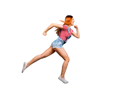 Full-size portrait of running sporty girl in a striped T-shirt and overalls who looks in front of her isolated on bright blue background