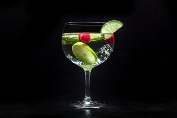Fancy cocktail with fresh fruit. Gin and tonic drink with ice at a party, on a black background. Alcohol with lime and raspberry - 761334006
