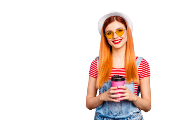 Cute young girl looks into the camera and holds pink paper glass with a drink in her hands isolated on bright blue background with copy space for text