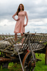 a young farmers wife in a pink dress stands on a horse trailer