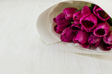 Bouquet of tulips in paper on a white wooden background