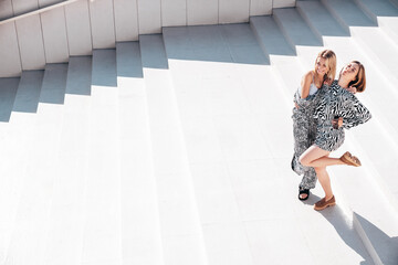 Two young beautiful smiling hipster women in trendy summer zebra print clothes. Carefree models posing in street. Positive models having fun. Cheerful and happy, at sunny day near wall.  Top view