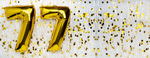 Golden foil balloon number, figure seventy-seven on white with confetti background. 77th birthday card. Anniversary concept. birthday celebration.