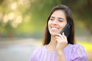 Happy woman walking talking on phone in a park