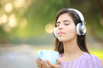 Relaxed woman with headphone meditating holding tea cup