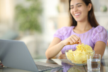 Happy woman watching movie on laptop eating potato chips - Powered by Adobe