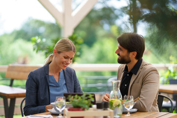 Business lunch for two managers, discussing new business project. Couple sitting outdoors on terrace restaurant, having dinner date.