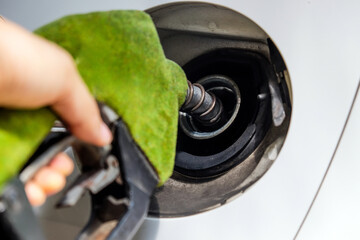 Close up image of hand refilling a car with fuel at a gas station, green fuel nozzle, energy concept