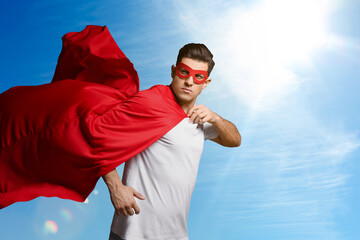 Man wearing superhero cape and mask against blue sky, space for text