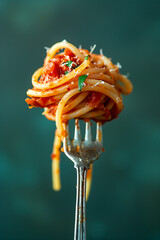 Italian spaghetti twirled around on a fork with meaty bolognaise sauce, isolated against a graduated teal background with copyspace.