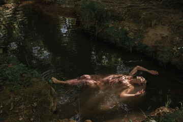 Woman submerged in the river water floating relaxed. Concept of spiritual connection with the natural environment and ethereal atmosphere between two worlds.