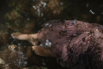 Close-up shot of the bare feet of a woman in a pink dress in the thermal water of the lake. Concept of spiritual connection with the natural environment and ethereal atmosphere between two worlds.