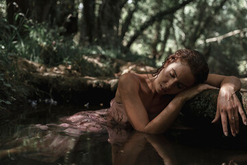 A young woman rests exhausted on a rock in the river. Concept of spiritual connection with the natural environment and ethereal atmosphere between two worlds.