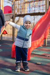 adorable baby boy playing at outdoor playground.kid climbing stairs,net fence, running, making funny faces,upset or happy,smiling or with tongue out. slide or swing in background, child having fun.